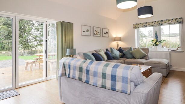 A modern living room with a sofa, a coffee table, and a lamp. There are two pendant lights and a window with curtains. - Bonnach (Muir of Ord)