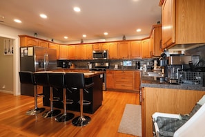 A modern kitchen with wooden cabinets, a stainless steel refrigerator, a microwave, and a coffee maker.