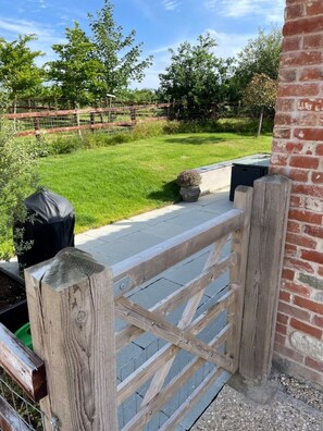 A wooden gate leading to a grassy area with a brick wall and a potted plant.
