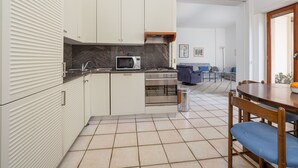 Una cocina compacta con muebles blancos, un microondas y una estufa. Hay una zona de comedor con una mesa de madera y sillas azules.