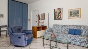 A living room with a blue sofa, a blue armchair, a glass coffee table, and a patterned sofa.