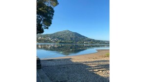 Ein Strand mit einem stillen See, einem Berg im Hintergrund und blauem Himmel.