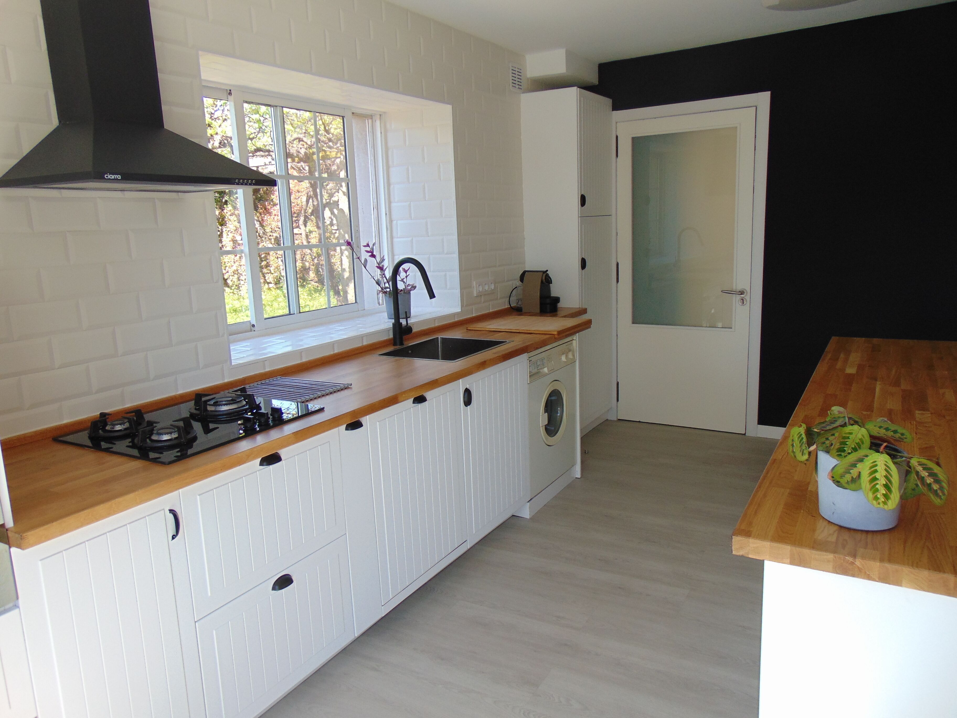 A compact kitchen with a gas stove, a sink, a dishwasher, and a window with a view of trees.
