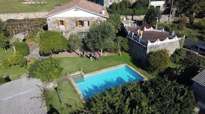 Una casa de piedra con piscina, rodeada de árboles y un muro de piedra.