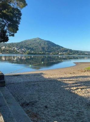 Una playa con un lago tranquilo, una montaña al fondo y un cielo despejado.