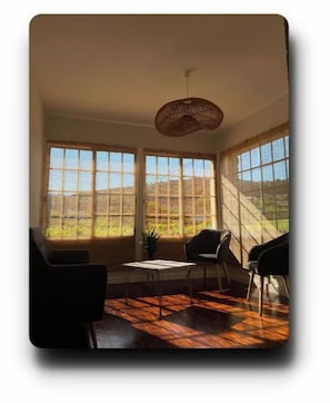 Una habitación con ventanas amplias, una lámpara colgante y dos sillones.