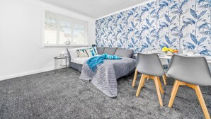 Une pièce moderne avec un tapis gris, un canapé gris, une table à manger avec des chaises et une fenêtre avec des stores.