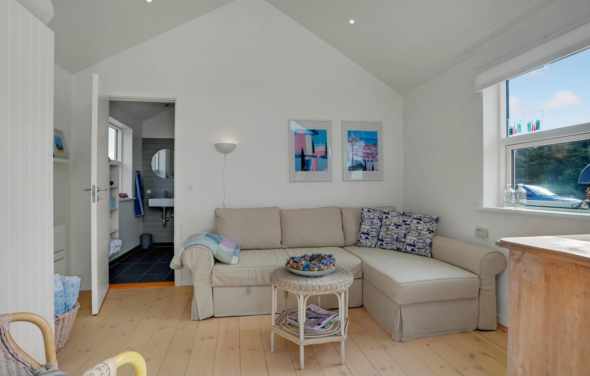 Ein gemütliches Wohnzimmer mit einer Couch, einem kleinen Beistelltisch und einem Fenster mit Blick ins Freie.