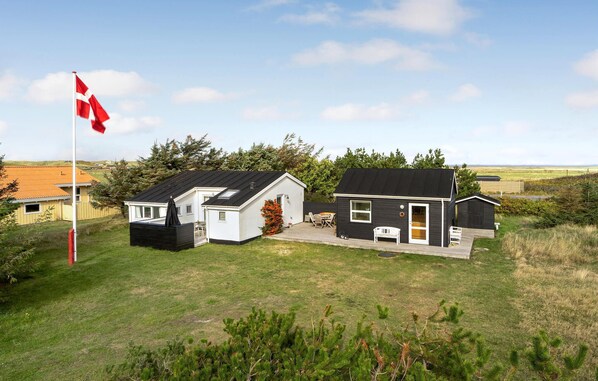 A small, two-story house with a black roof and white exterior, featuring a patio with outdoor furniture. - 3 bedroom nice home in Ulfborg (Ulfborg)