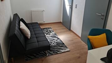 Un espai habitable reduït amb un sofà negre, una catifes amb estampat de zebra, una cadira color aquamarina i una taula blanca.