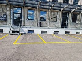 Un edificio con fachada de ladrillo, varias ventanas y un estacionamiento con líneas amarillas.