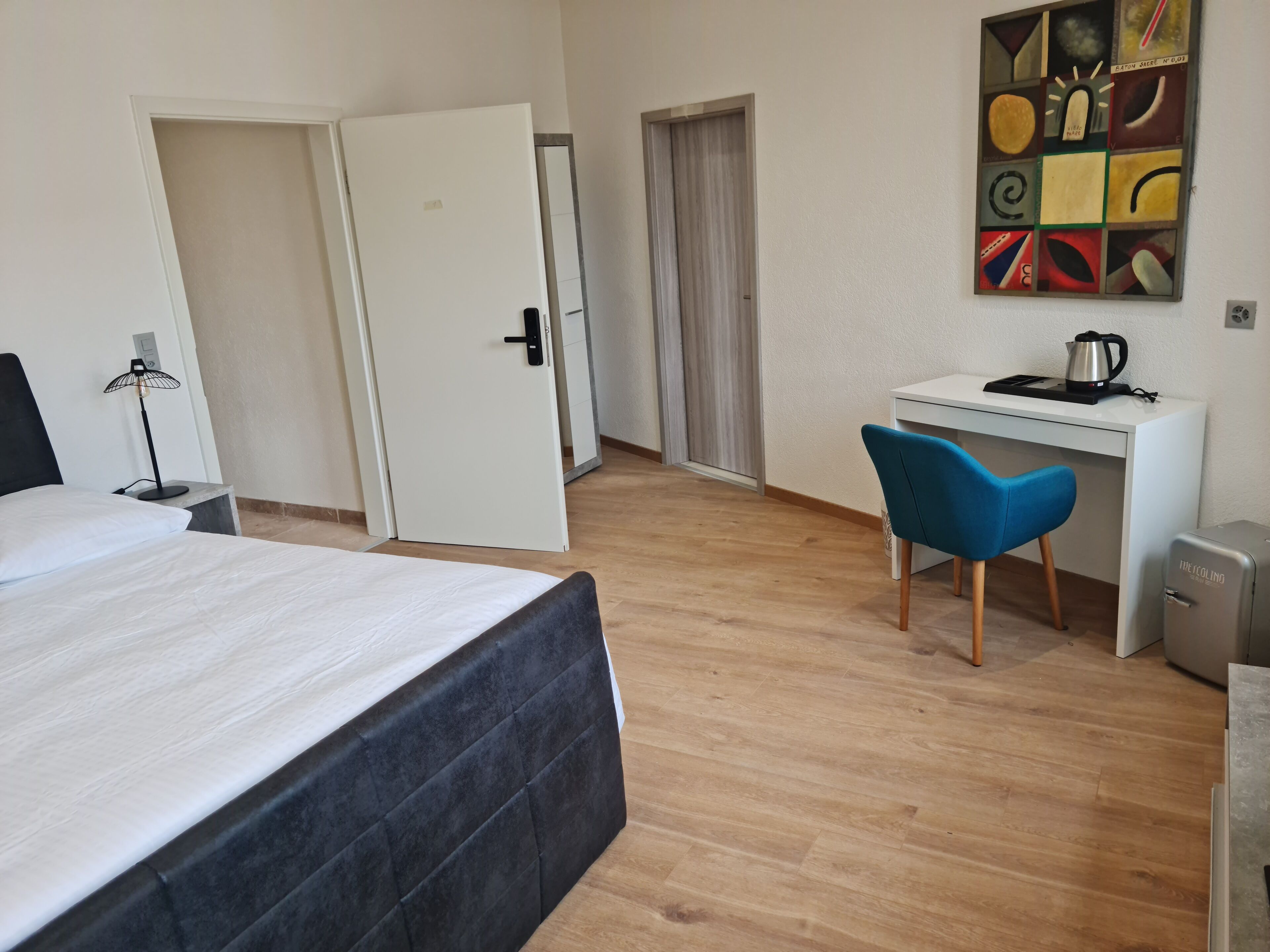 Ein Hotelzimmer mit Bett, Schreibtisch, Stuhl, Heizkörper und einem Wandbild.