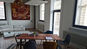 A modern living room with a wooden table, chairs, a sofa, and a large abstract painting on the wall. - LA FACTORY by LNA (Porrentruy)