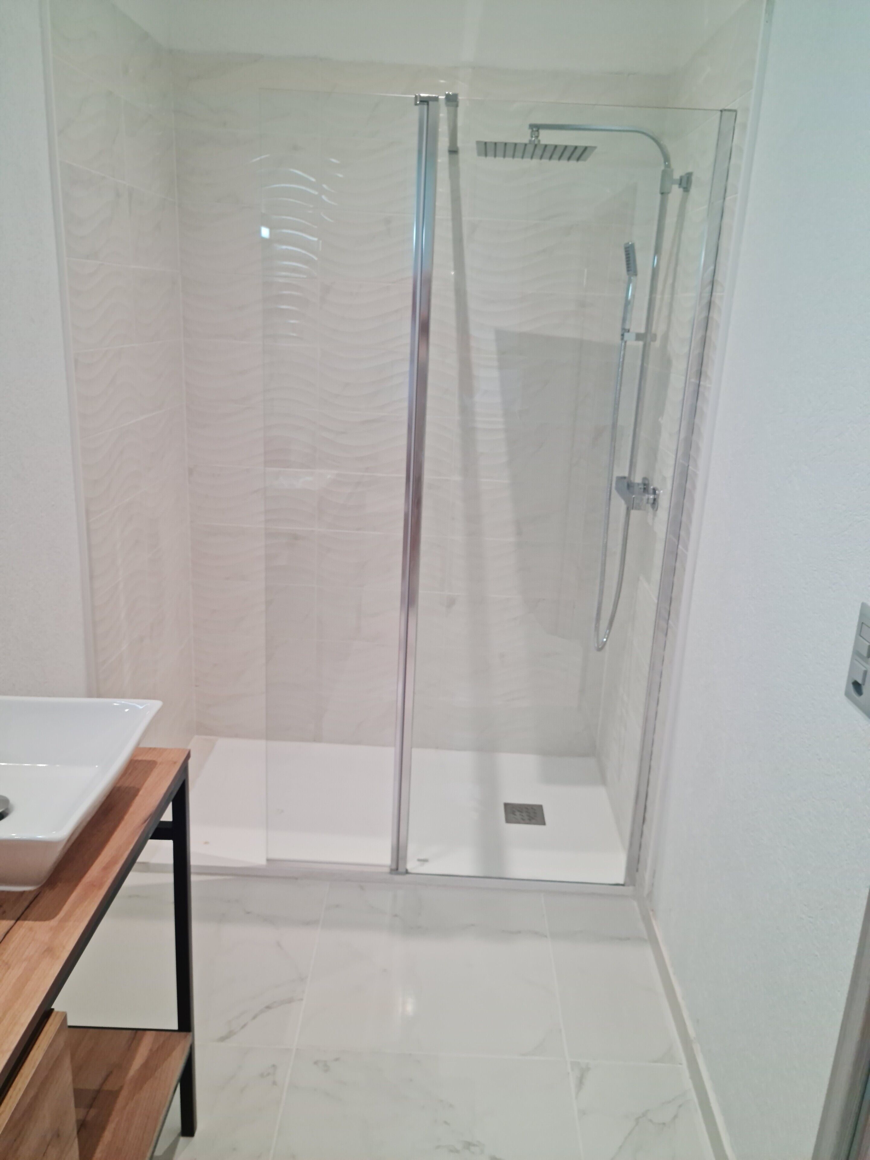 Une salle de bain moderne avec une douche à parois de verre, un meuble-lavabo en bois et un revêtement de sol en marbre.