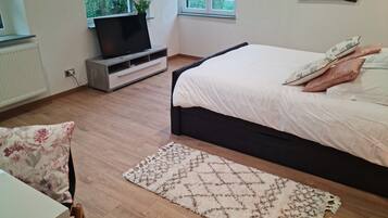 Une chambre à coucher avec un lit, un téléviseur posé sur un meuble, une fenêtre et un radiateur.