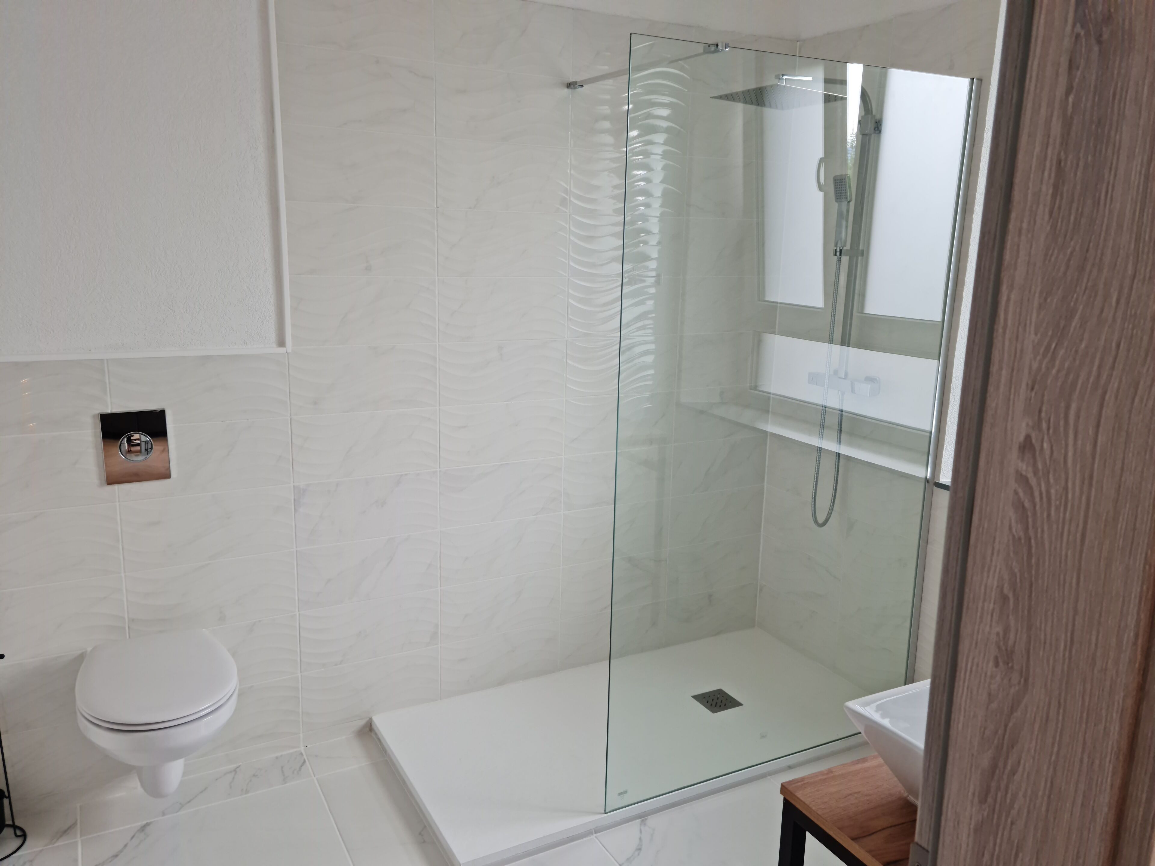 Un bagno moderno con cabina doccia in vetro, un water bianco e un mobile lavabo in legno.