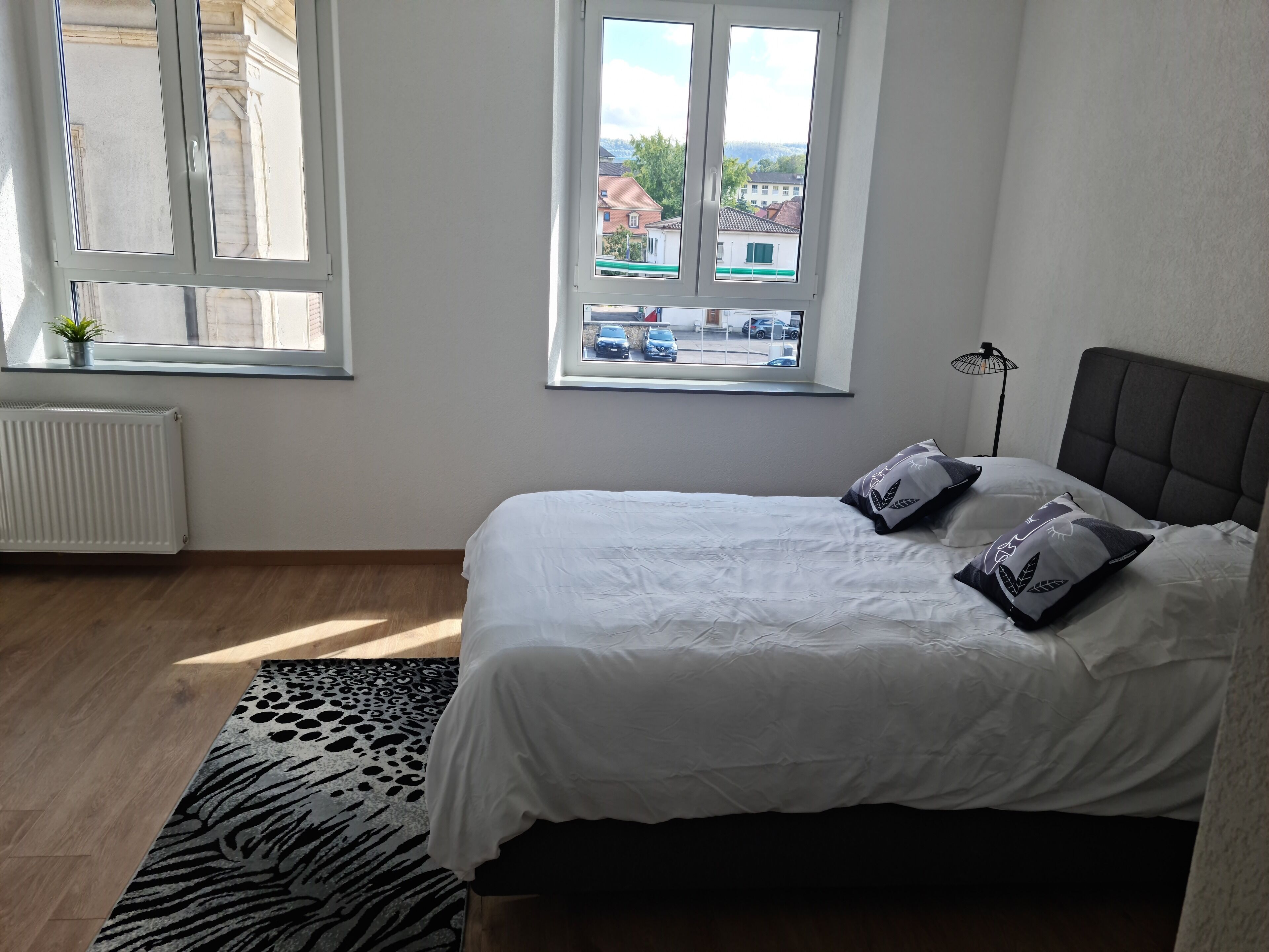 A bedroom with a bed, a window, a radiator, and a zebra-patterned rug.