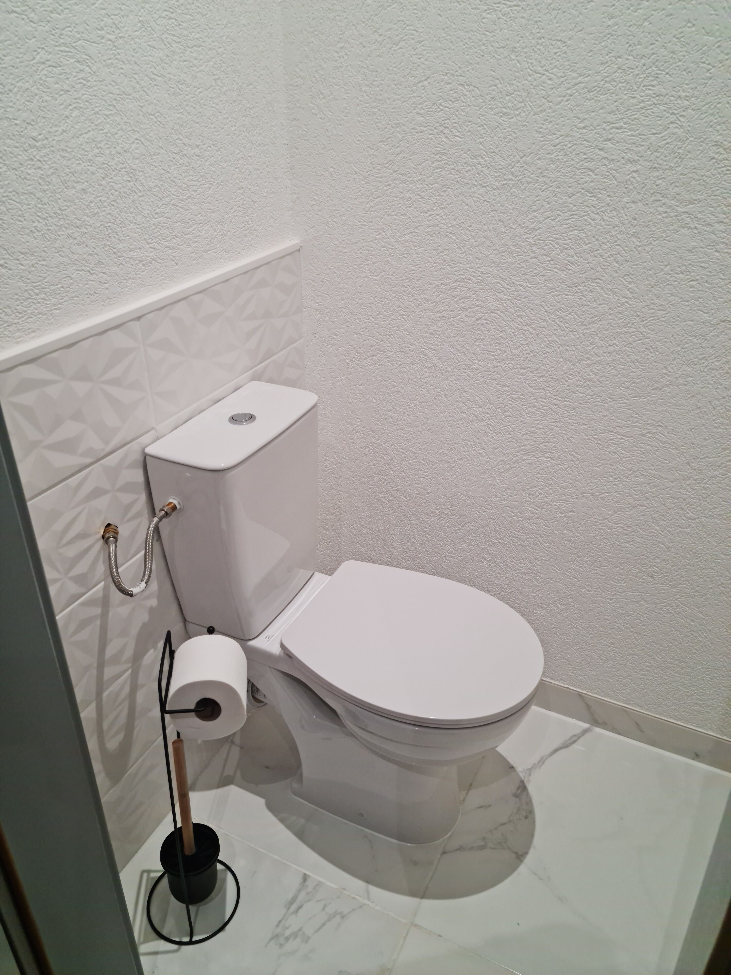 Eine weiße Toilette mit Boden in Marmoroptik und einer strukturierten Wand.