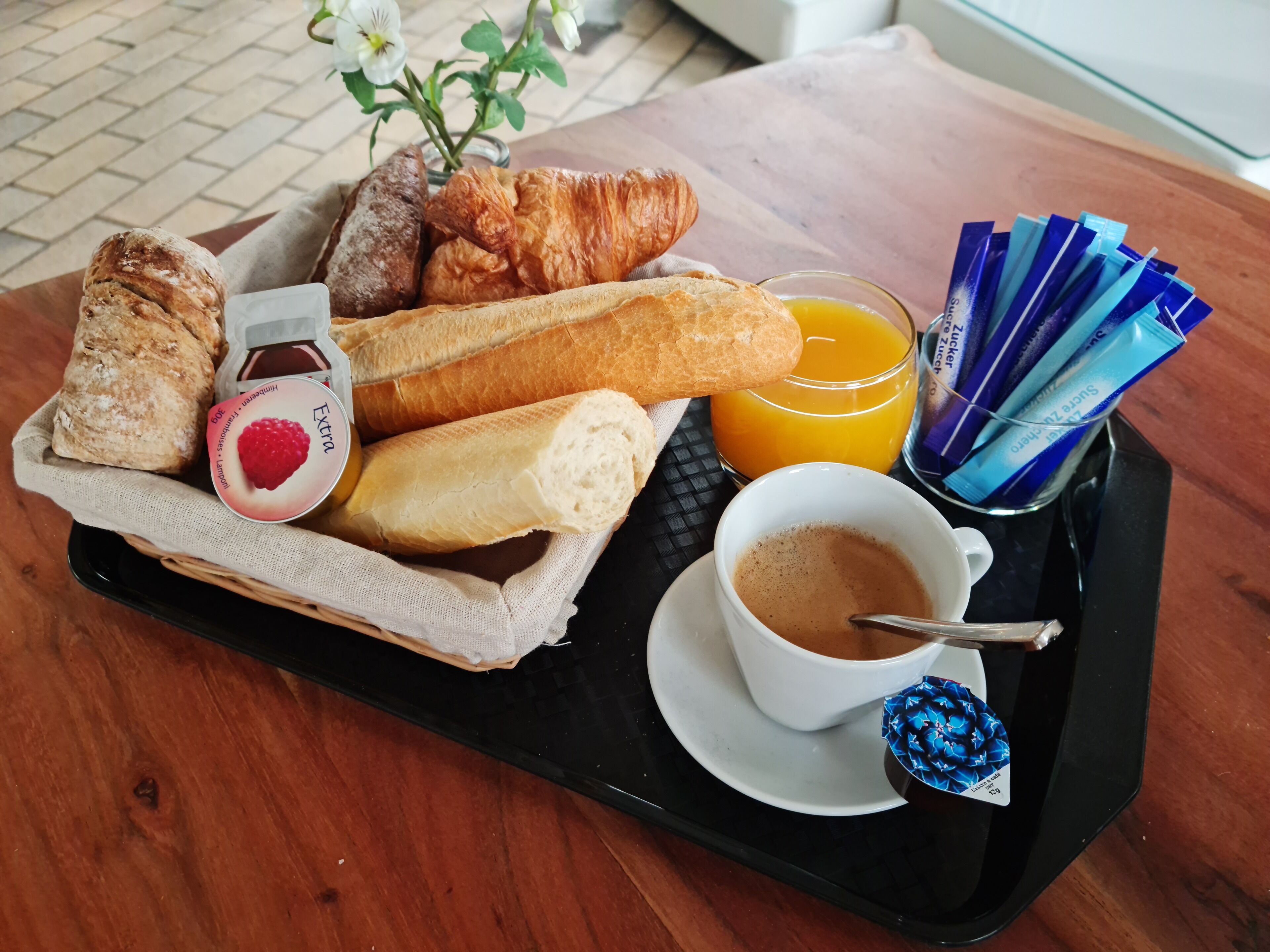 A tray with croissants, a baguette, a jar of jam, a glass of orange juice, and a cup of coffee.