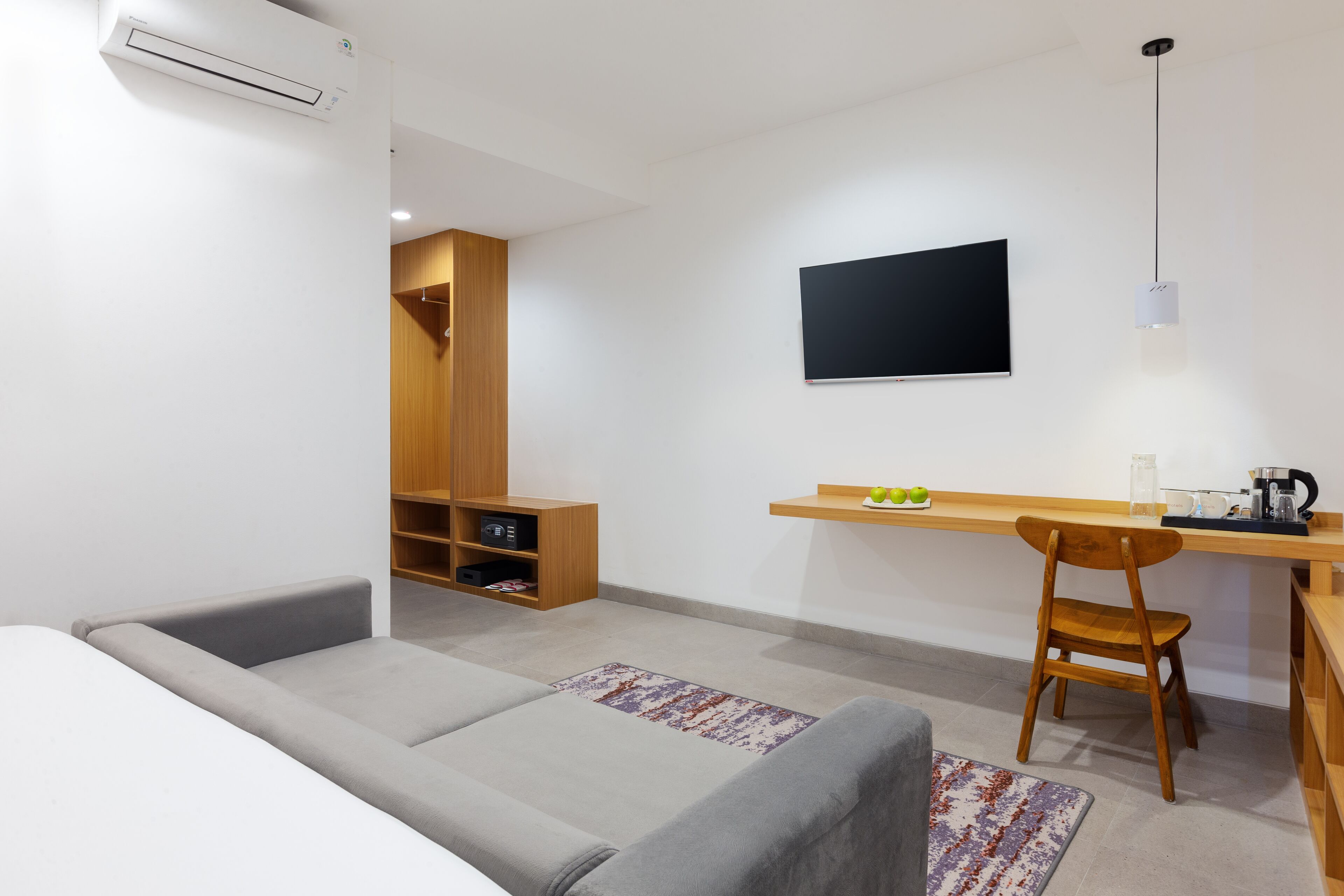 Una habitación moderna con un sofá gris, un escritorio de madera, un televisor montado en la pared y un estante con objetos.