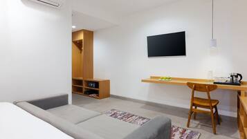 Una habitación moderna con un sofá gris, un escritorio de madera, un televisor montado en la pared y un estante con objetos.