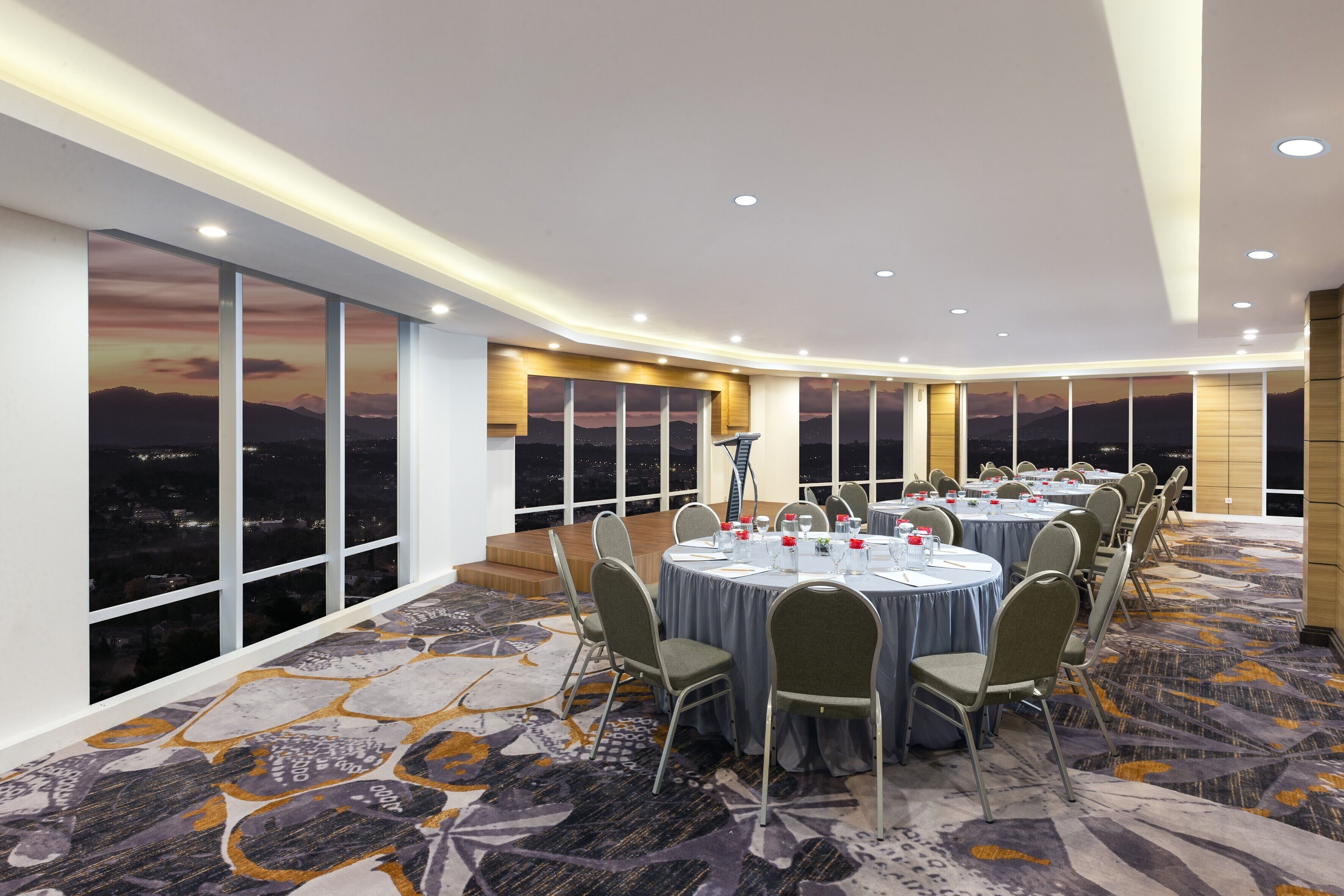 A conference room with round tables, chairs, and a panoramic city view through large windows.