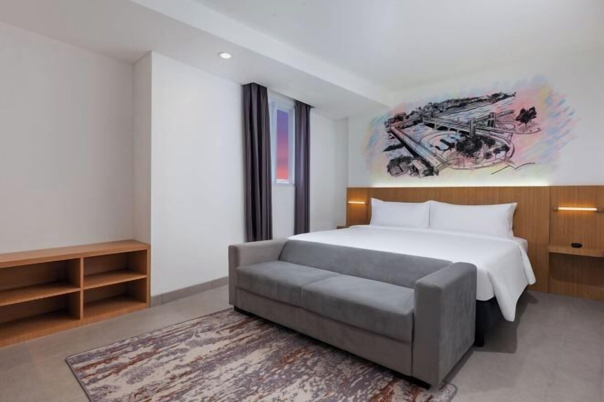 Ein modernes Hotelzimmer mit einem großen Bett, einem grauen Sofa, einem gemusterten Teppich und Wandbildern.