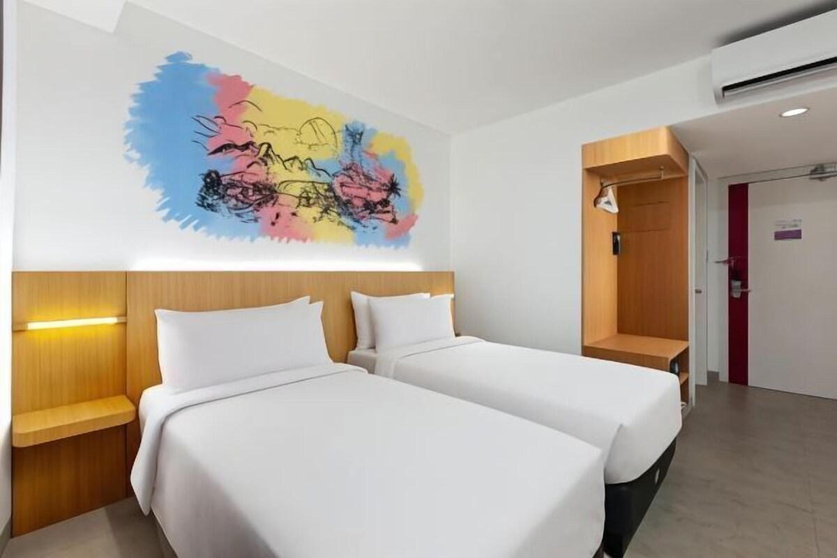 Ein Hotelzimmer mit zwei Betten, einem hölzernen Kopfteil, einem Wandbild und einem Kleiderschrank.