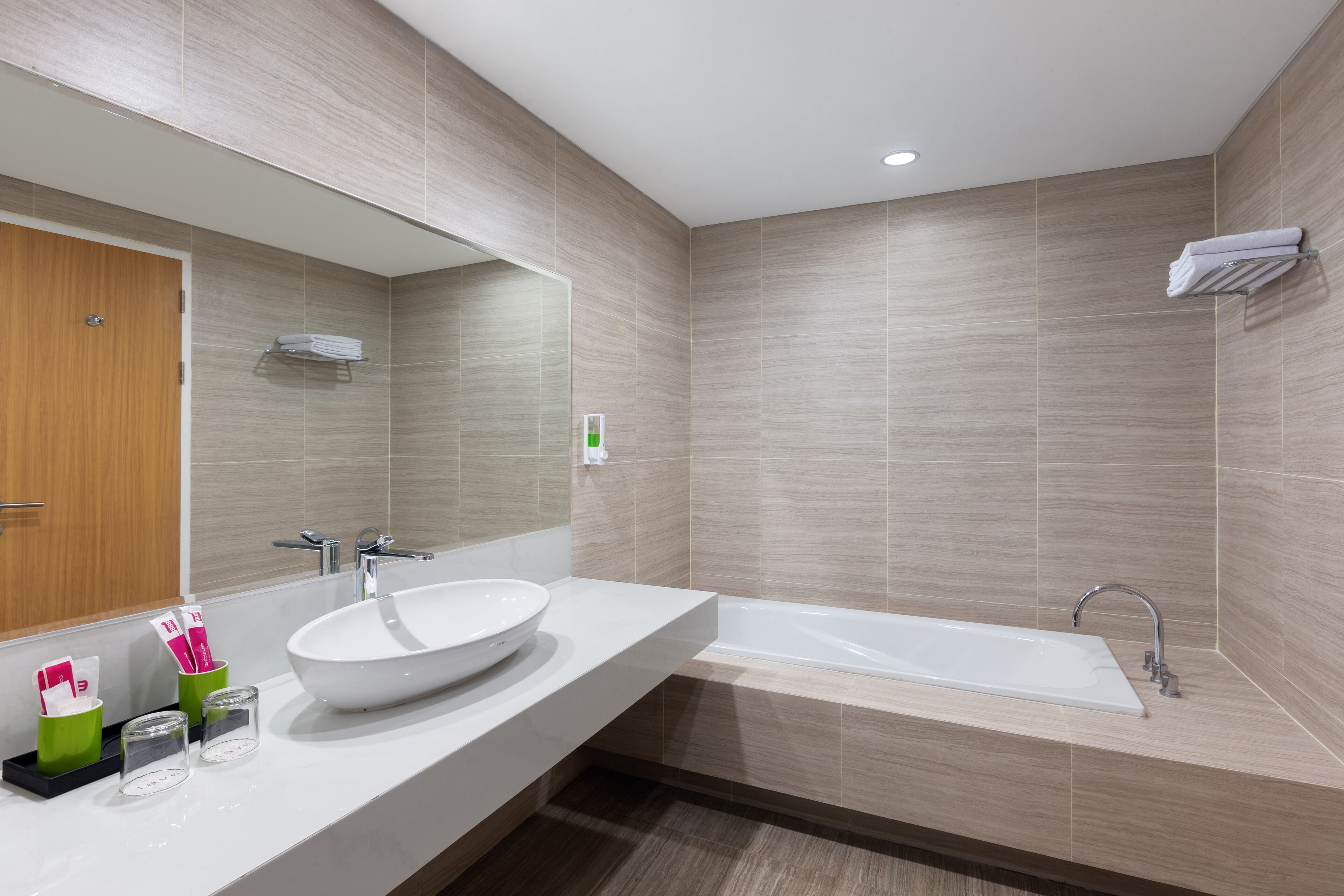 Un baño moderno con un espejo grande, un lavabo redondo, una bañera y una puerta de madera.