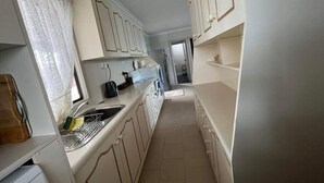 Una cucina piccola con mobili bianchi, un lavandino e una finestra con tende in pizzo.