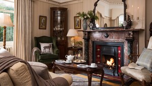 A traditional room with a fireplace, green armchairs, a table with tea set, and a cabinet with glass doors. - Ardtara Country House (Maghera)