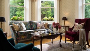 A cozy living room with a floral sofa, a red armchair, and a coffee table with tea set. - Ardtara Country House (Maghera)