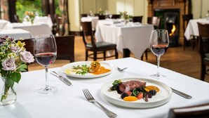 A dining area with tables set for meals, wine glasses, and a vase with flowers. - Ardtara Country House (Maghera)
