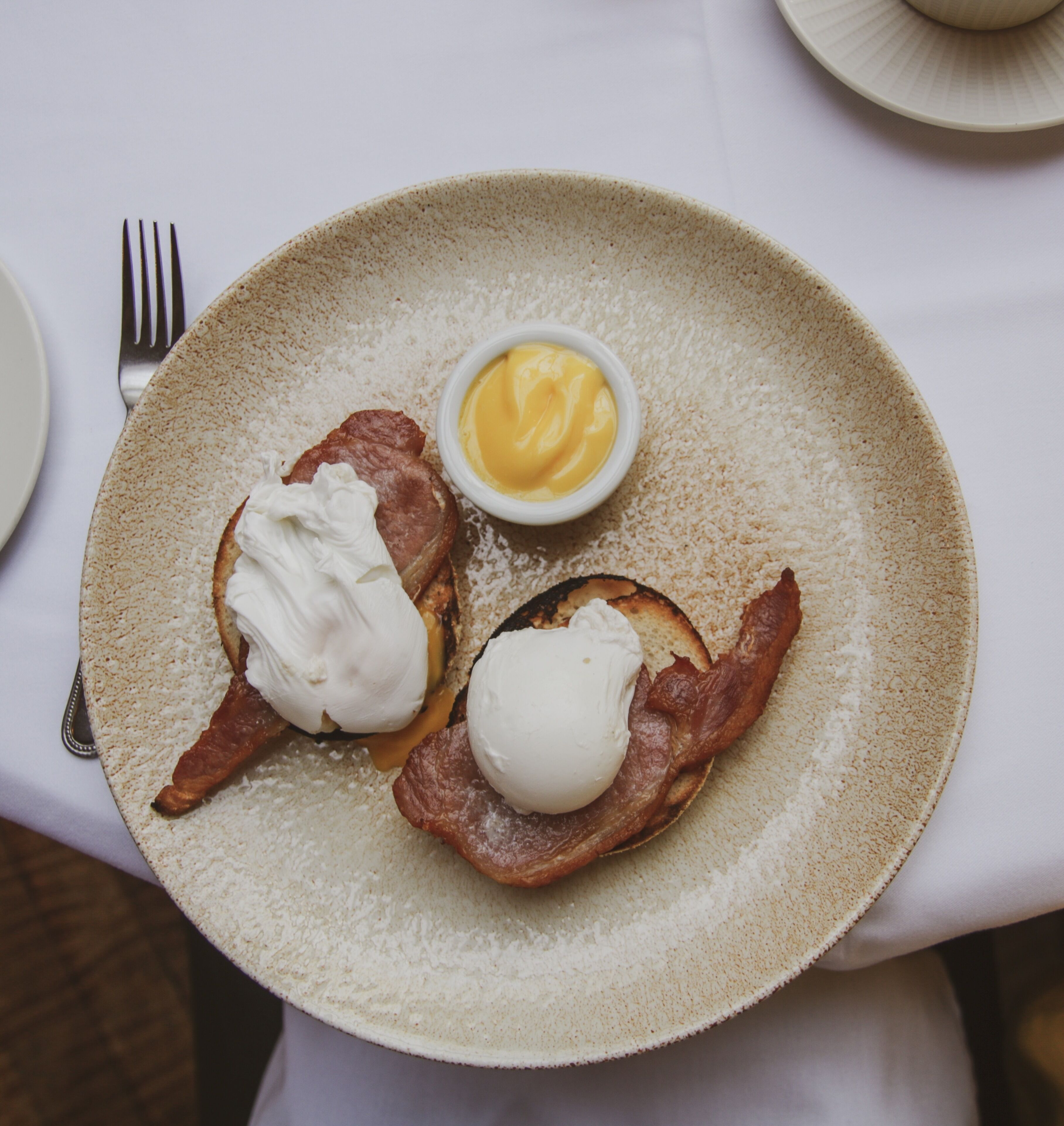 A plate with two poached eggs on toast, accompanied by a small bowl of hollandaise sauce.