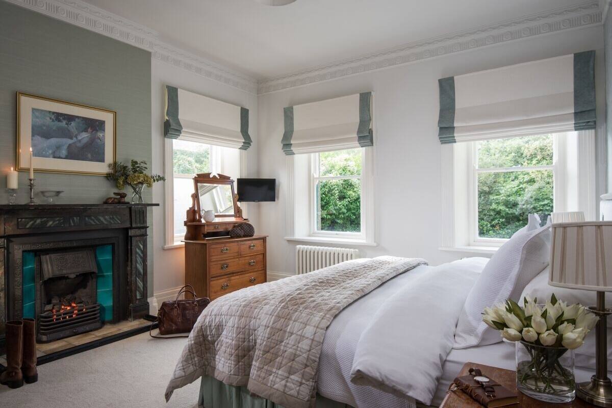 A bedroom with a fireplace, a bed, a dresser, and a television.