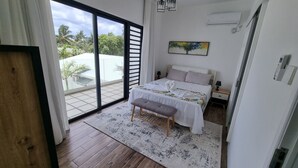 A bedroom with a bed, bench, and a view of the outdoors through a sliding door. - Villa with pool 5 minutes from the beach! (Trou-aux-Biches)