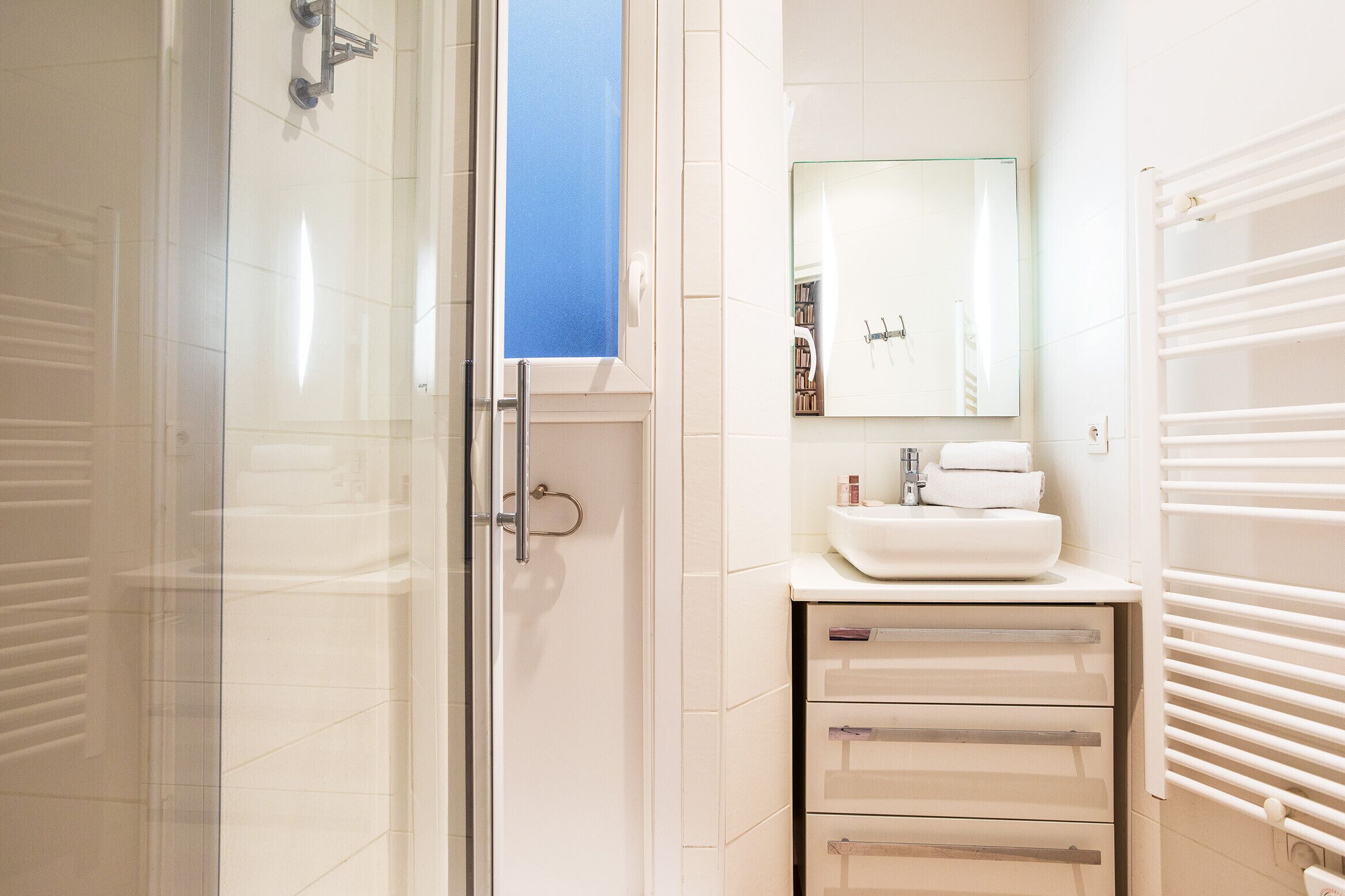 A modern bathroom with a glass shower enclosure, a white sink with a mirror above it, and a towel rack.