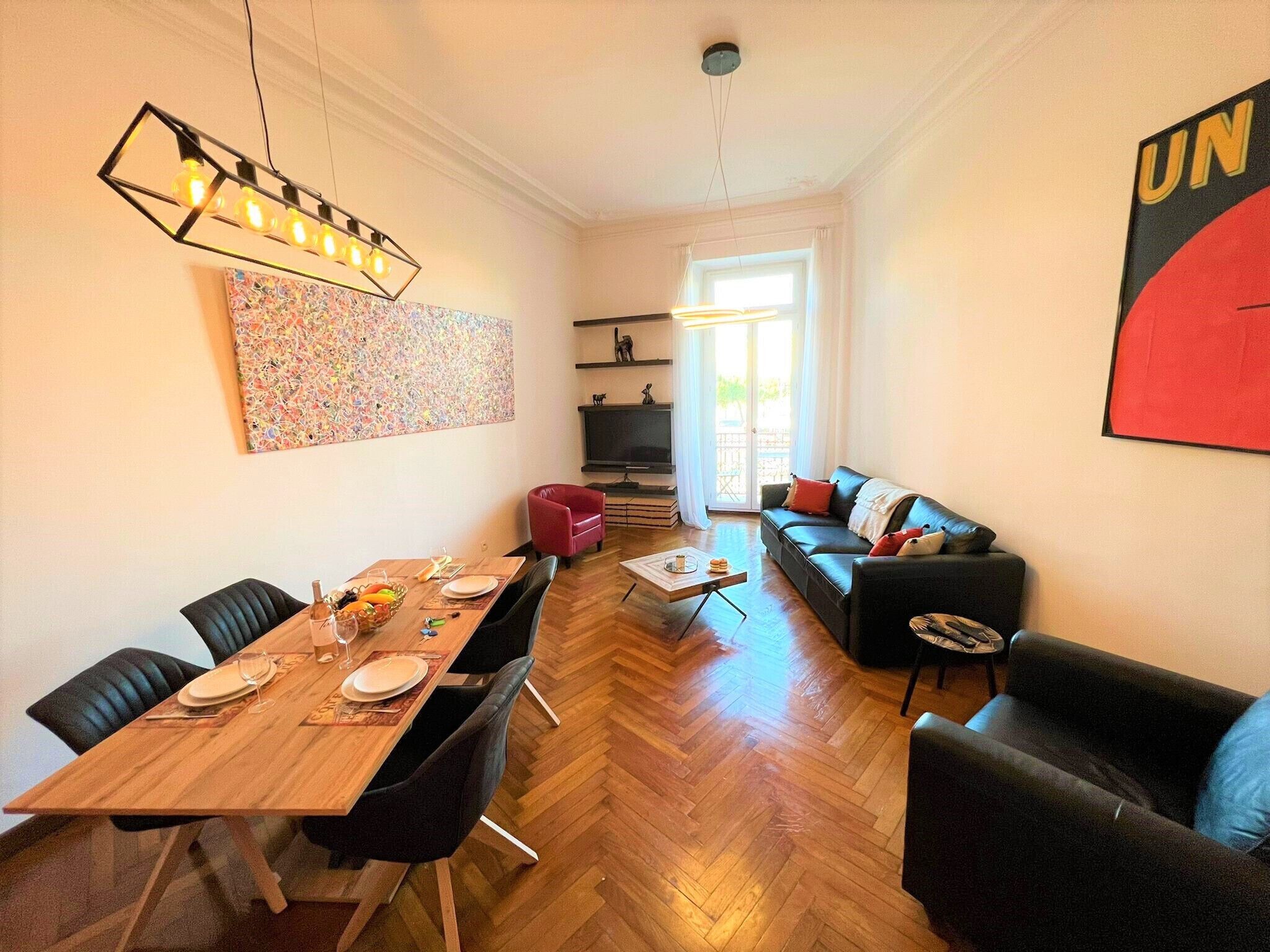 Un salon moderne avec une table à manger en bois, des canapés en cuir noir et un grand tableau abstrait accroché au mur.