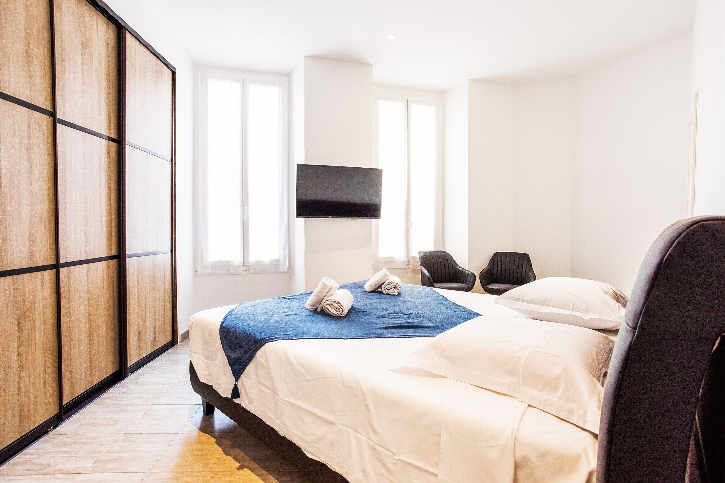 Ein Hotelzimmer mit Bett, Wandfernseher, Sessel und Kleiderschrank.