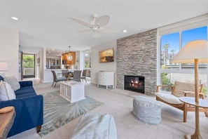 A spacious living room with a fireplace, a dining area, and a kitchen in the background.