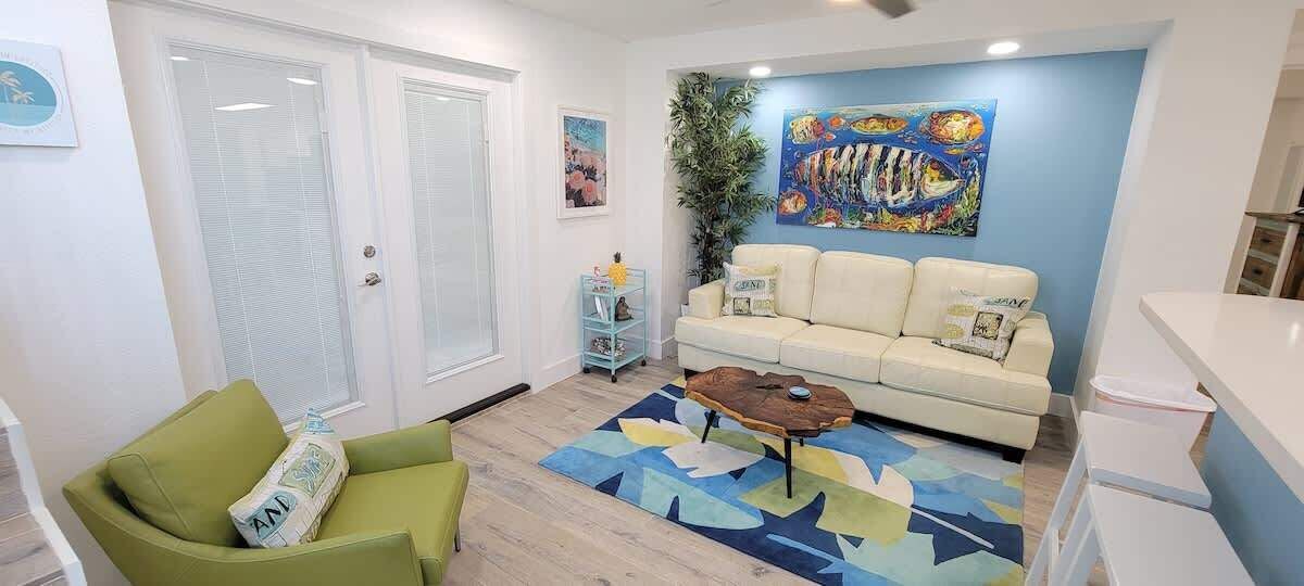 A living room with a green armchair, a beige sofa, a coffee table, and a colorful rug.