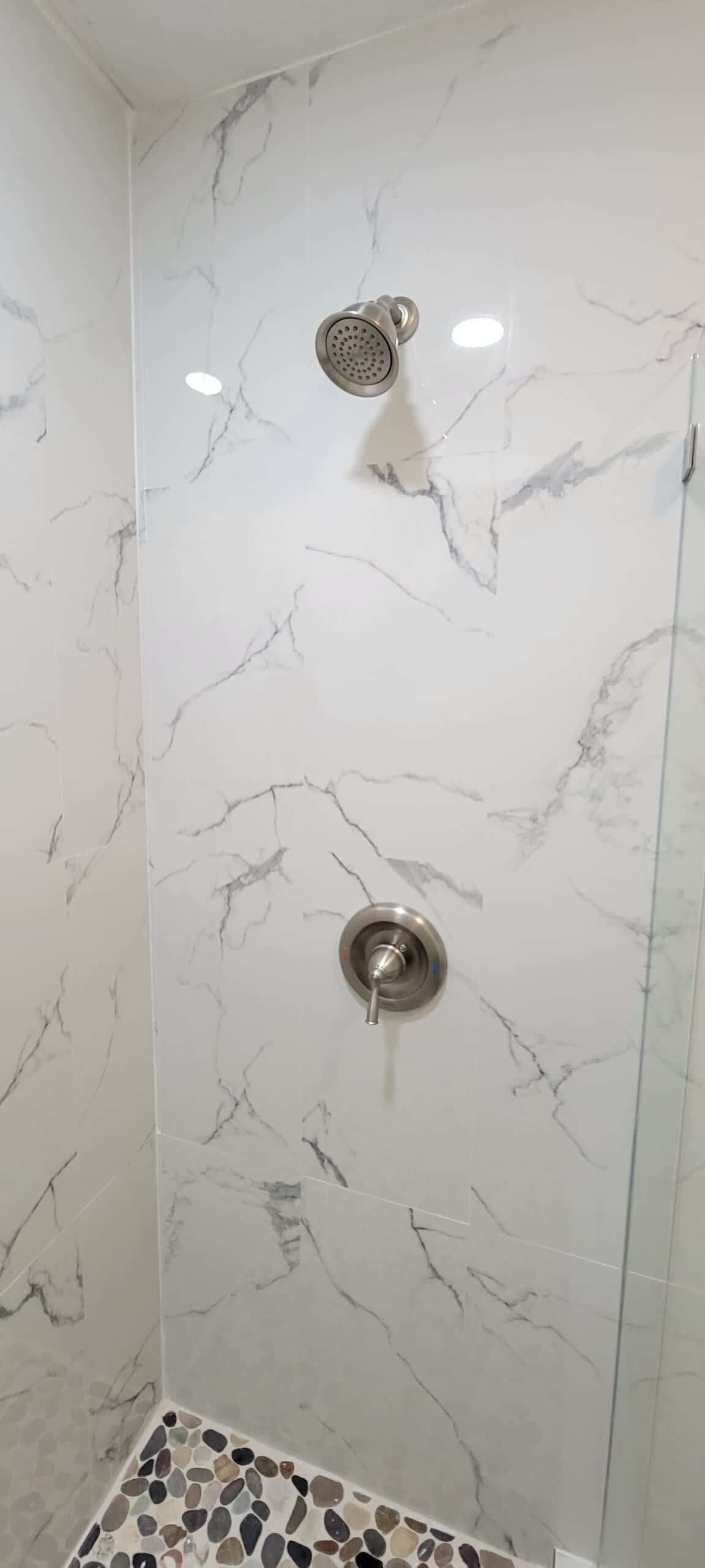 A shower with a glass door and marble tiles.