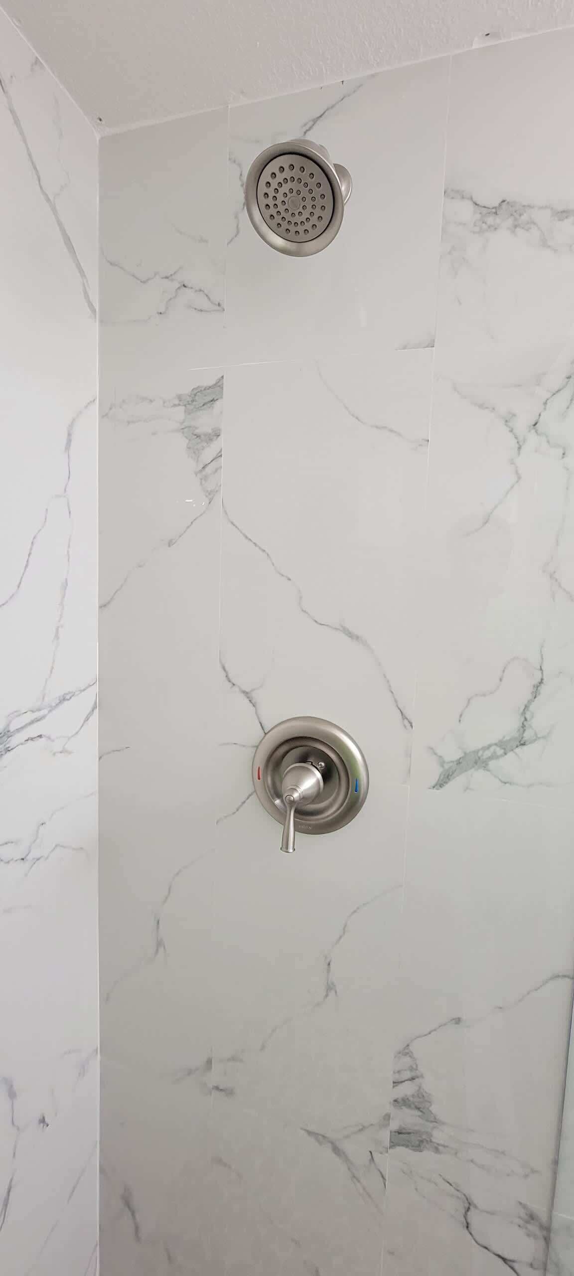 Ducha con desagüe circular y cabezal de ducha de mano, frente a una pared con azulejos tipo mármol.