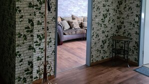 Une pièce avec un mur dont le motif imite des briques, un plancher en bois, un canapé agrémenté de coussins à motifs, une petite table ronde et un lampadaire.
