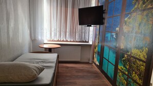 Une petite pièce agréable, avec un lit, une table et un téléviseur fixé au mur.