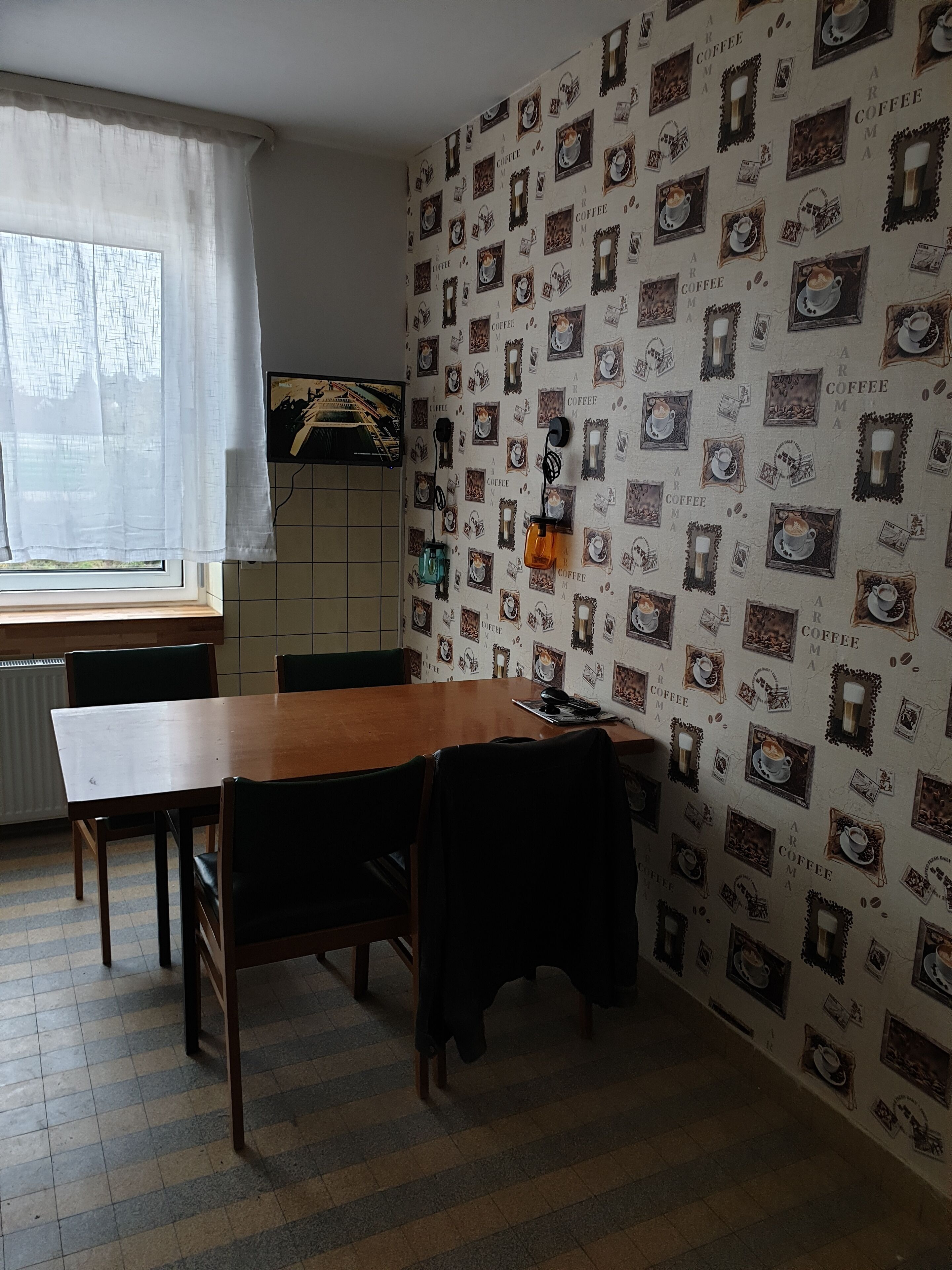 Un'area pranzo con un tavolo e sedie in legno, una finestra con tende bianche e un muro decorato con immagini a tema caffè.