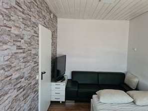 Una habitación con pared de piedra, un armario blanco con cajones, un sofá negro y una cama con almohadas.