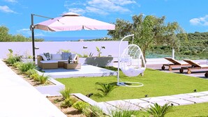 A modern outdoor seating area with a sofa, a hanging chair, and lounge chairs, overlooking a scenic landscape. - Stavento Luxury Villa Private Pool (Chania)