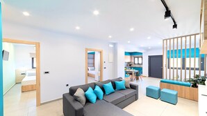 A modern living room with a grey sectional sofa, blue cushions, and a dining area with a table and chairs. - Stavento Luxury Villa Private Pool (Chania)