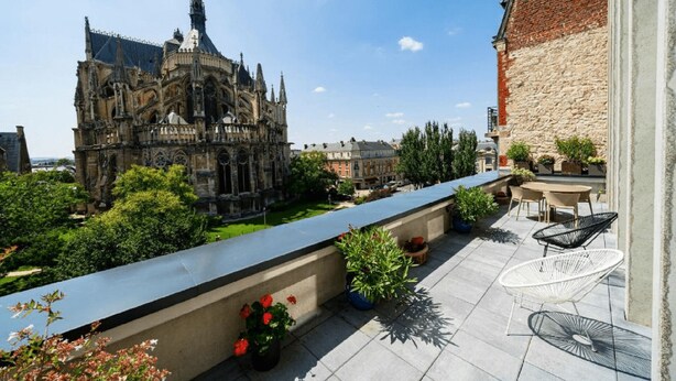 Une terrasse sur le toit offrant une vue sur un bâtiment historique, avec des sièges en plein air et des plantes en pot.